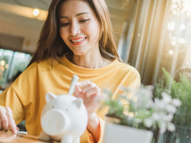 女性が笑顔で貯金箱にお金を入れようとしている写真。